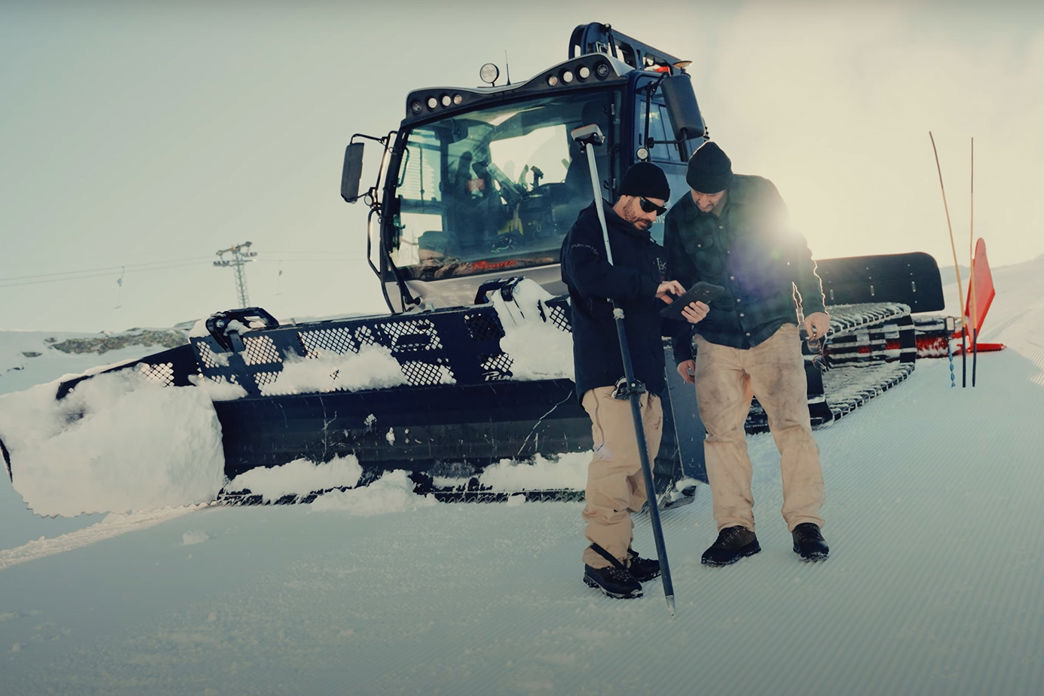 Zwei Männer vor einer Pistenraupe bei der Vorbereitung der Skipiste für die FIS Freestyle WM 2025.