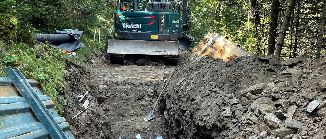 Bagger beim Aushub einer Trasse im Wald bei Laax – Vorbereitung für Erdverlegung einer Hochspannungsleitung.