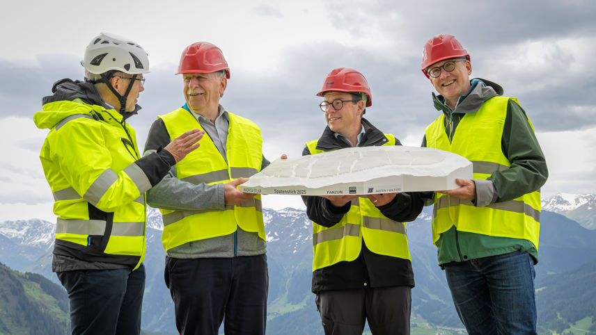 Vier Männer mit Schutzwesten und Helmen präsentieren ein Modell beim Spatenstich Madrisa Solar 2025 in den Bündner Bergen.