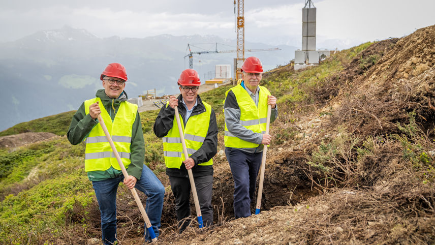 Spatenstich für das Projekt Madrisa Solar mit drei Verantwortlichen in Schutzkleidung und Bauhelmen auf der Baustelle.